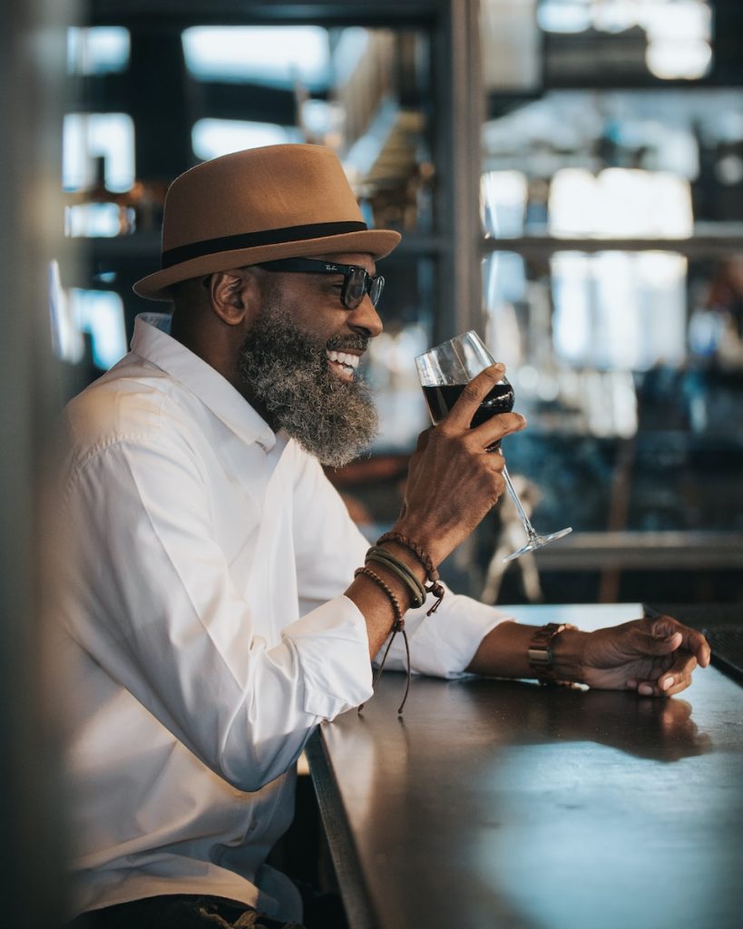 man in white dress shirt and brown hat drinking wine